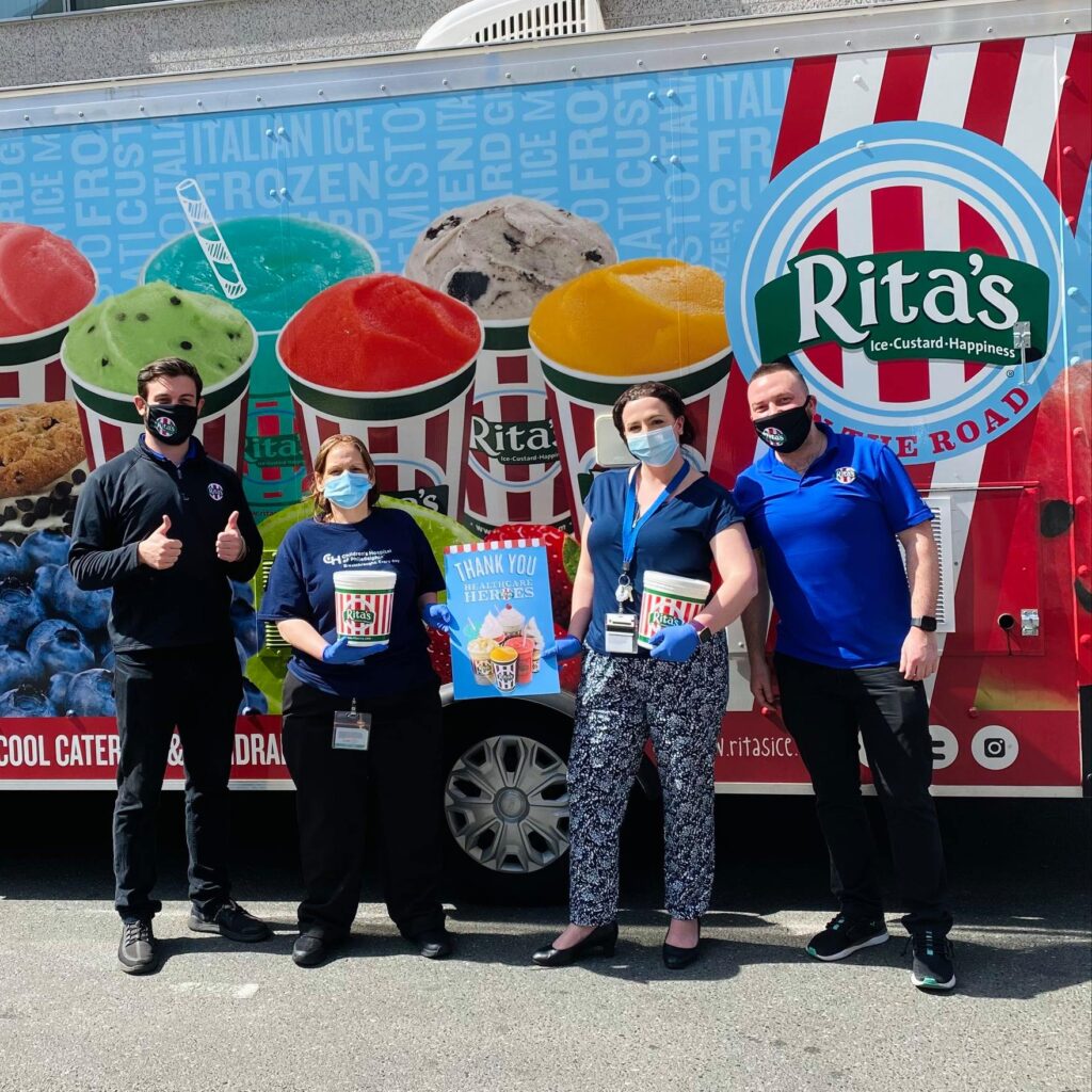 A group of people in COVID-safe masks pose in front of a Rita's Italian Ice truck